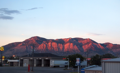 [The sun sets in front of the mountains and on this evening it backlit the mountains giving the rocky surface a red-orange tint.]